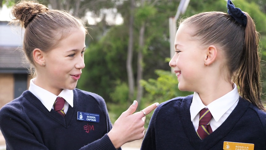 Two girls wearing school uniforms turning towards each other and laughing.
