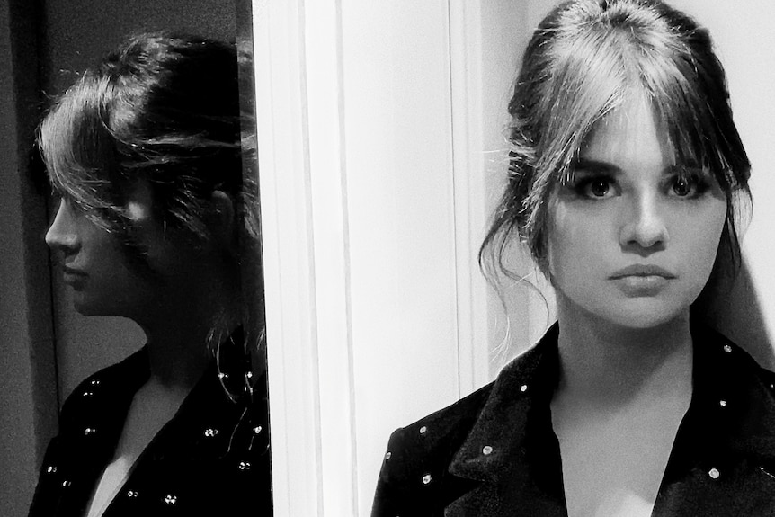 A black and white photo of Selena looking at the camera with her reflection mirrored on the side.