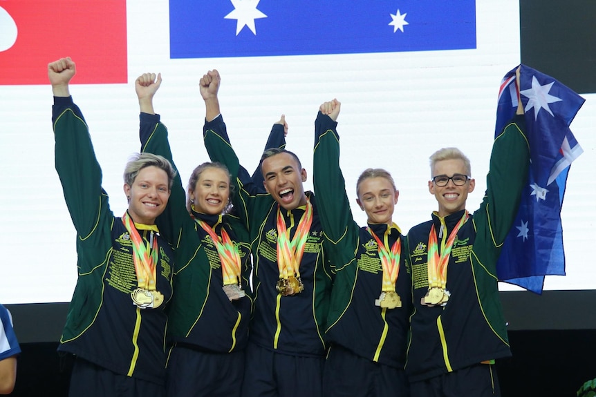 Five people in Australian tracksuits put their arms in the air and cheer.