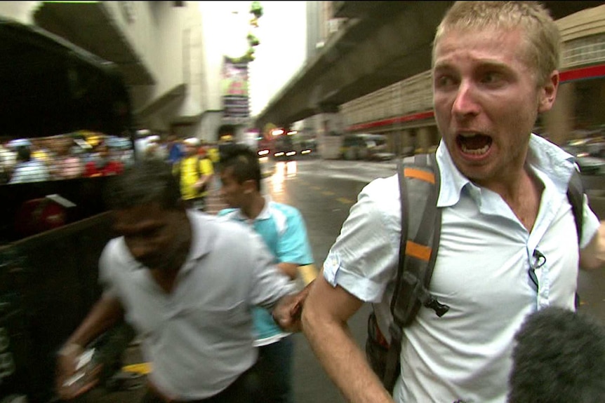 Macdonald covering a riot in unknown location looking scared as though running away.