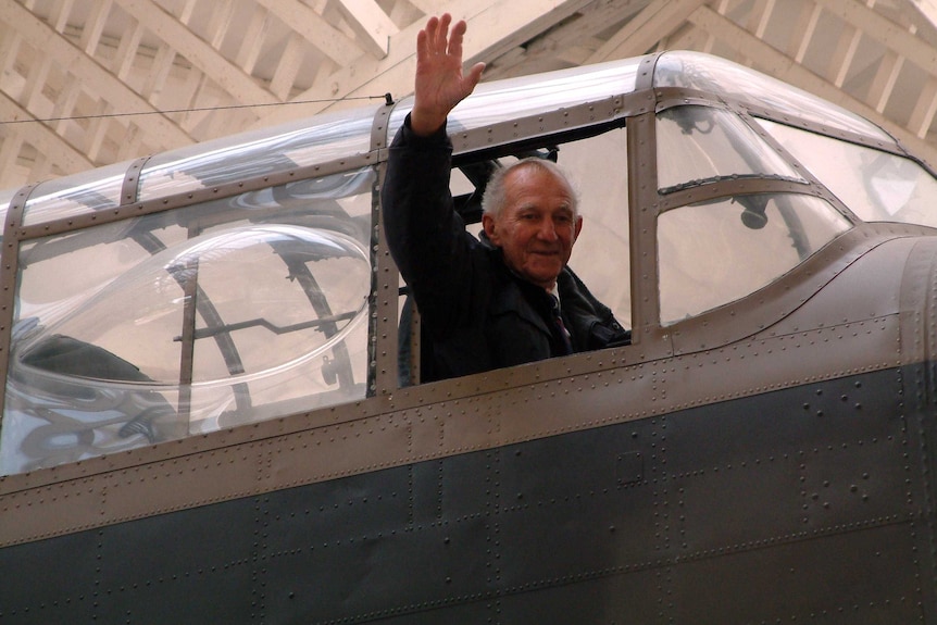 A man waves out of the window of a plane.