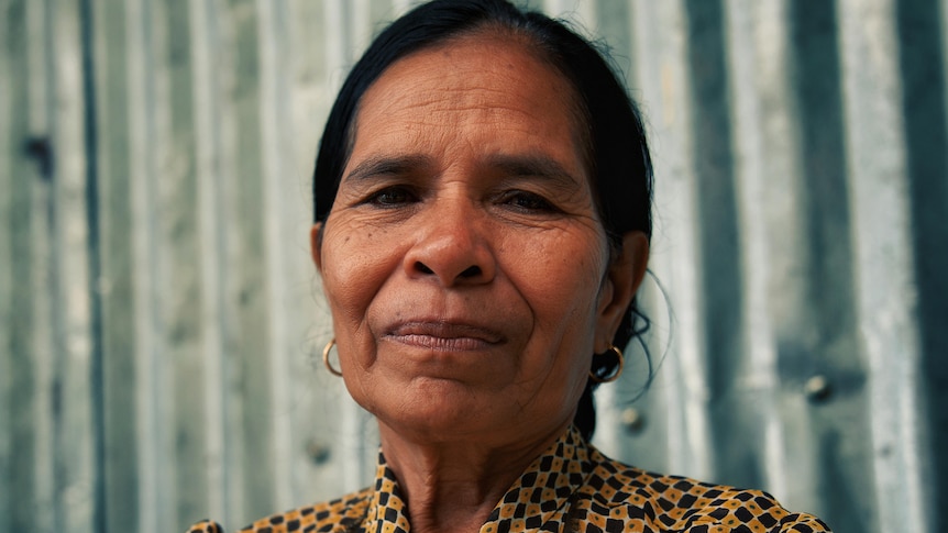 A Timorese woman with dark hair wearing a yellow and brown checkered blouse