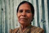A Timorese woman with dark hair wearing a yellow and brown checkered blouse
