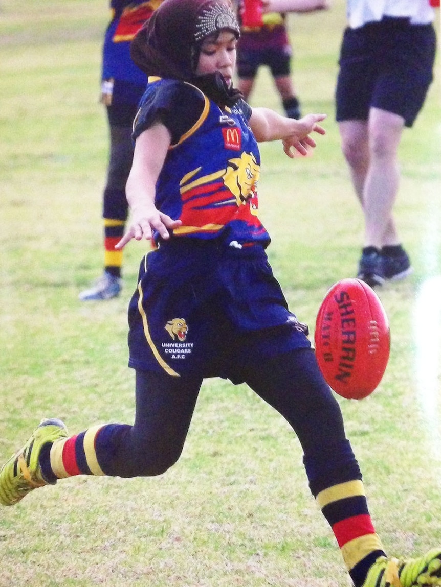 10-year-old Afghani refugee Zimra Hussain kicking an AFL football in Toowoomba on Queensland's Darling Downs