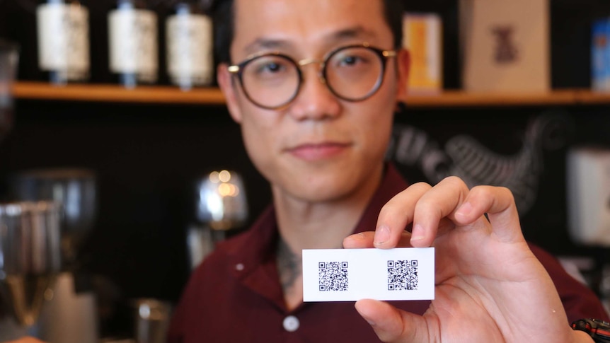 Cafe owner Ben Kim holds a card showing the address to his digital wallet