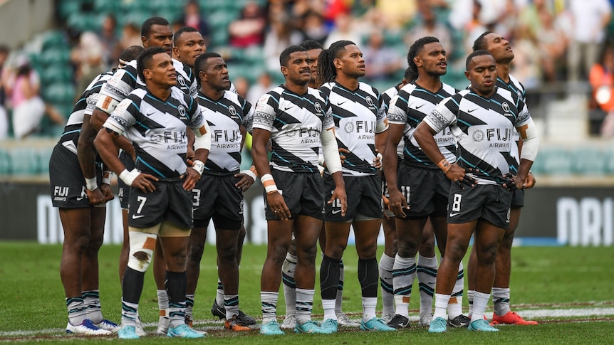 Fijian rugby sevens players stand on the field together.
