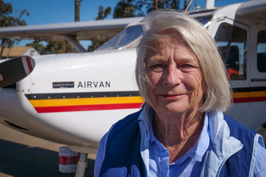 Older woman in blue shirt stands in front of small aircraft called Airvan