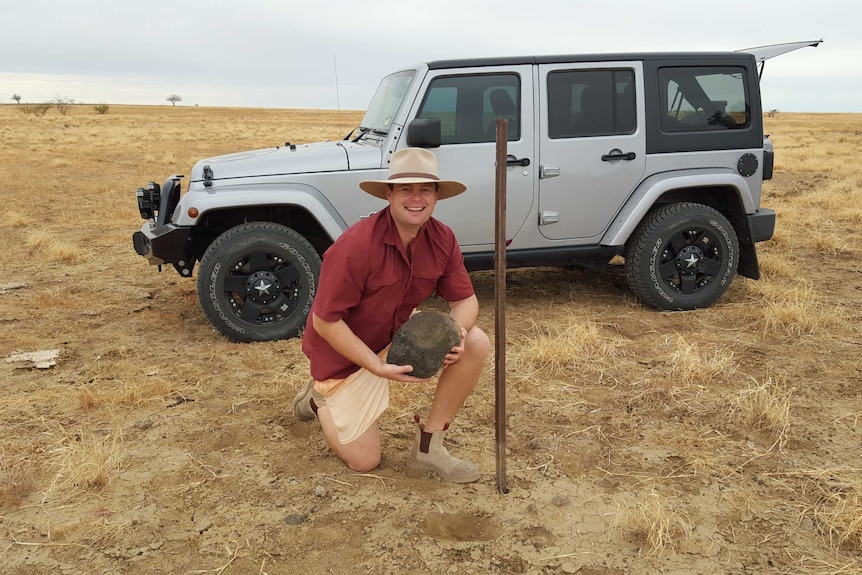 Dr Matt White kneels in front of a car in a paddock at Winton.