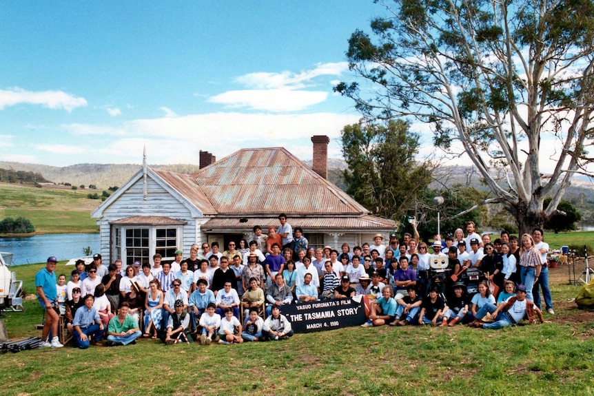 Cast and crew sit stand in front of house