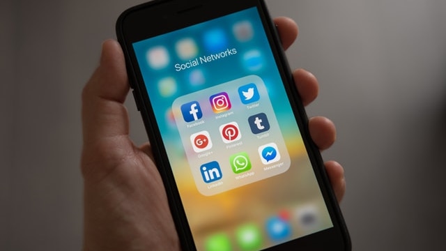 A picture of a hand holding a phone with a number of social media apps on it.