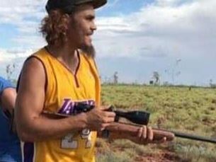 an Indigenous man holds a rifle in the bush