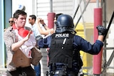 Man holds his hand up to police officer who is wielding a baton