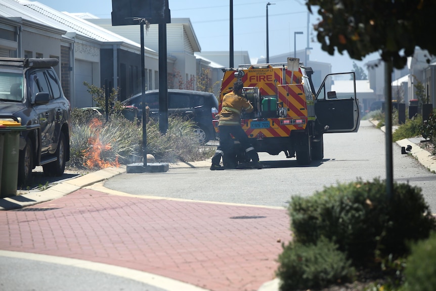 A firefighter puts out a spot fire on a verge right outside a residential home