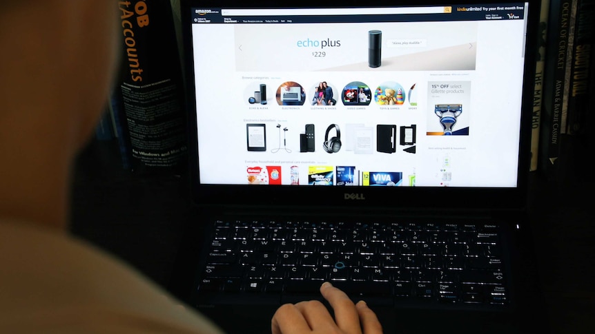 A shot looking over the shoulder of a woman using a black laptop to shop on Amazon.