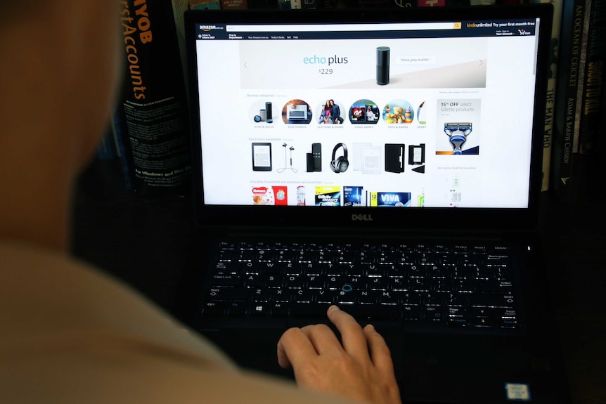 A shot looking over the shoulder of a woman using a black laptop to shop on Amazon.