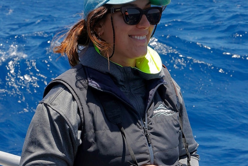 A woman on a boat smiles with blue ocean water behind her.