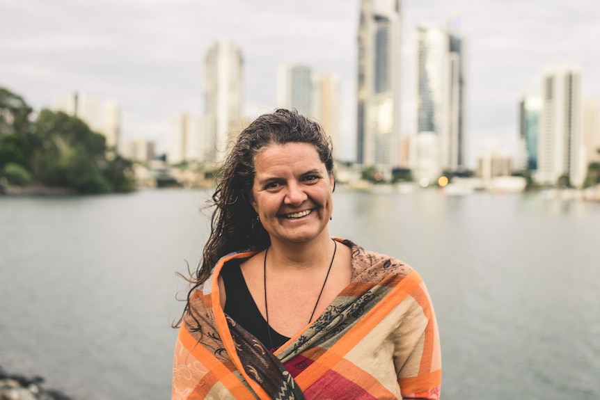 A woman stands smiling in front of Gold Coast high-rise towers in the background
