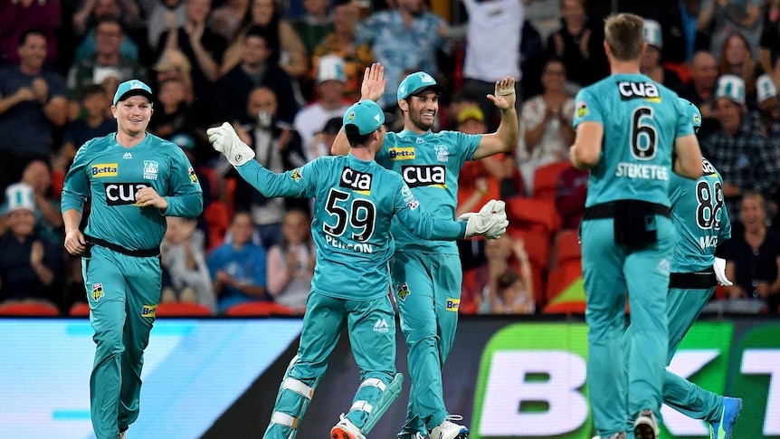 A Big Bash player high-fives teammates to celebrate a wicket as the crowd cheers in stands behind.