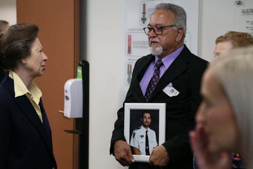 a woman speaks to man holding a picture of a young man