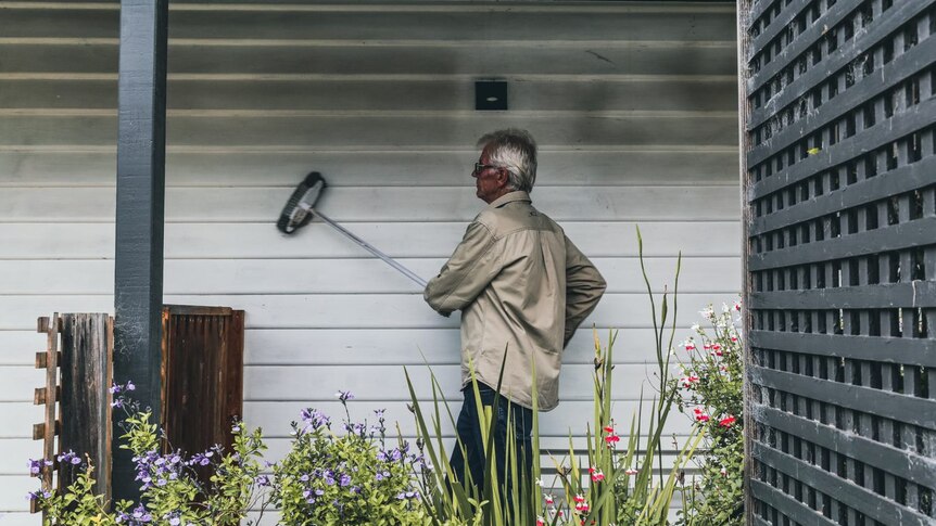 Robert Richards brushes dust from his weatherboard home
