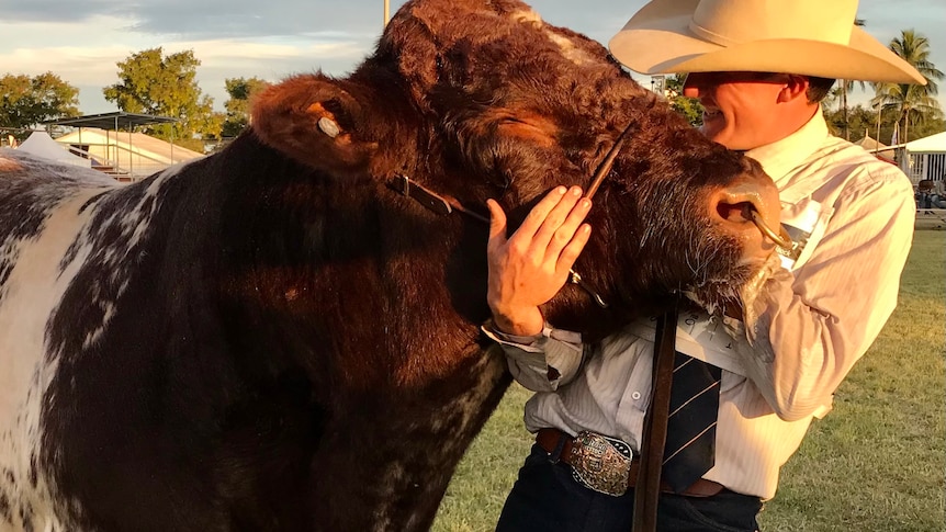 A young man hugging the head of a brown bull.