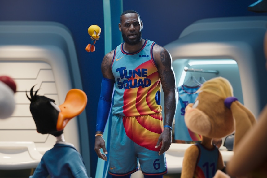 A surprised LeBron James talks to animated characters wearing basketball uniforms, including Tweety and Daffy Duck 