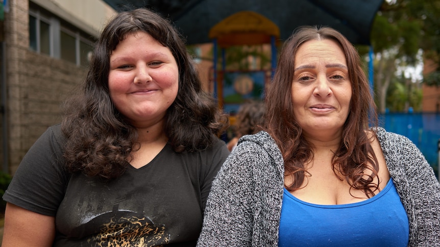 Annette and her teenage daughter Hannah pictured outside a community centre, smiling slightly.