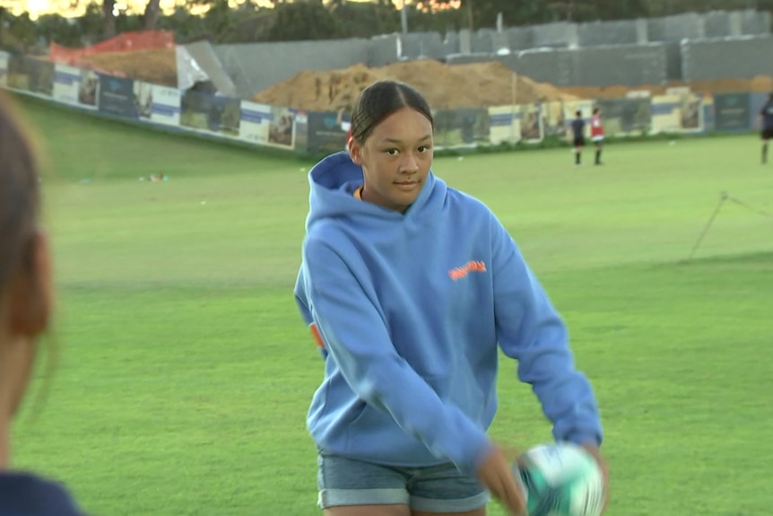 A young girl named Kaiya Puki in a blue hoodie getting ready to throw a rugby ball.