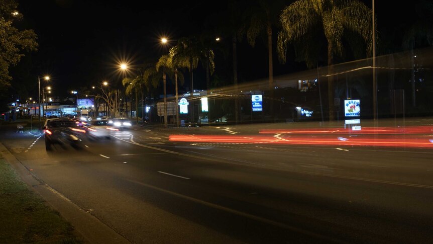 A series of motel signs along a road, with a streak of car lights going past.