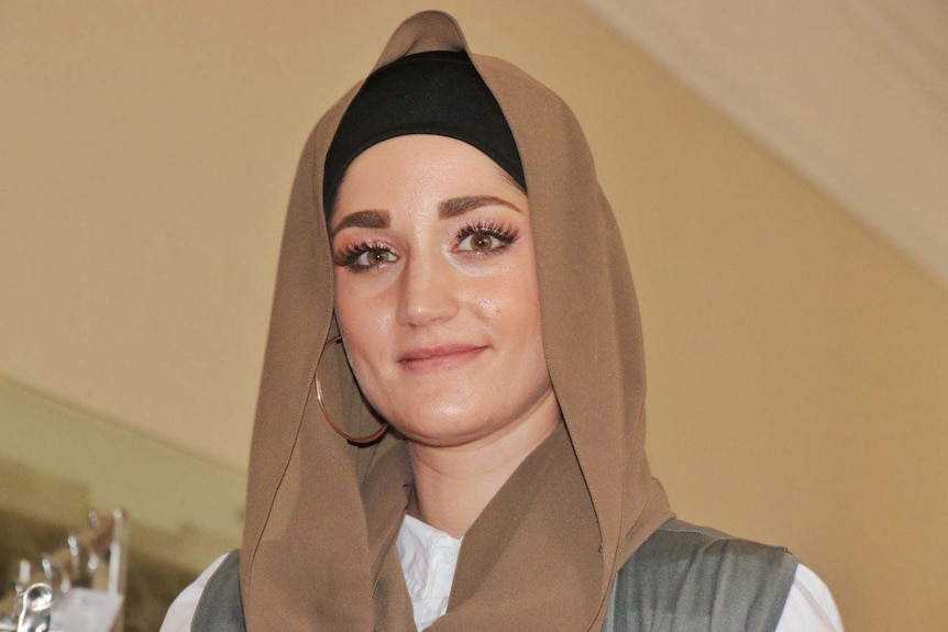 Sureyya wears a head covering and big hoop earings, and smiles at the camera.