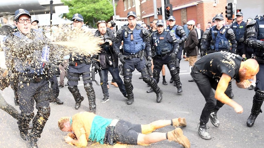 Protesters clash with police in Kensington, with on officer spraying capsicum spray while a man lies on the ground.