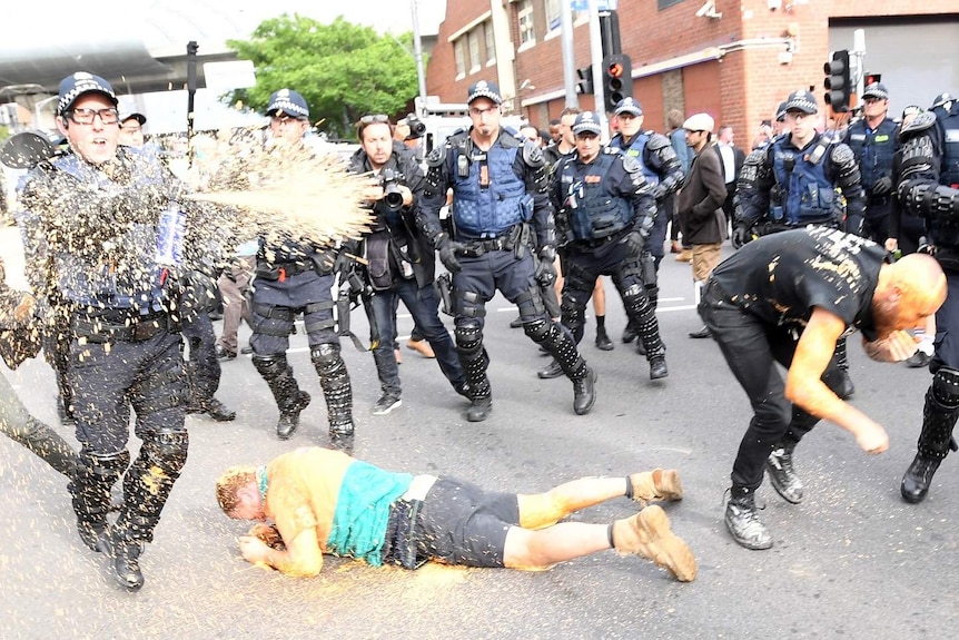 Protesters clash with police in Kensington, with on officer spraying capsicum spray while a man lies on the ground.