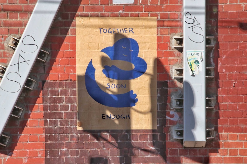 An poster with a blue graphic depicting two people hugging with the words "Together Soon Enough" on a brick wall in Melbourne.