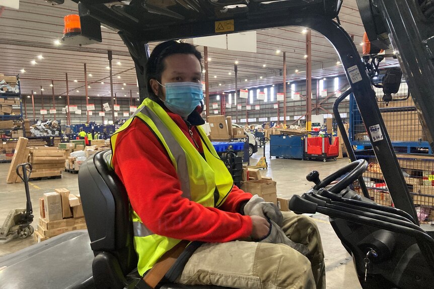 A man seated on a forklift, wearing a mask and high-vis vest.
