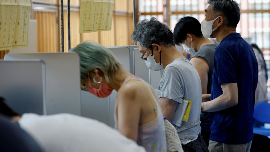 voters in face masks cast their ballots for the Japanese upper house election in a room