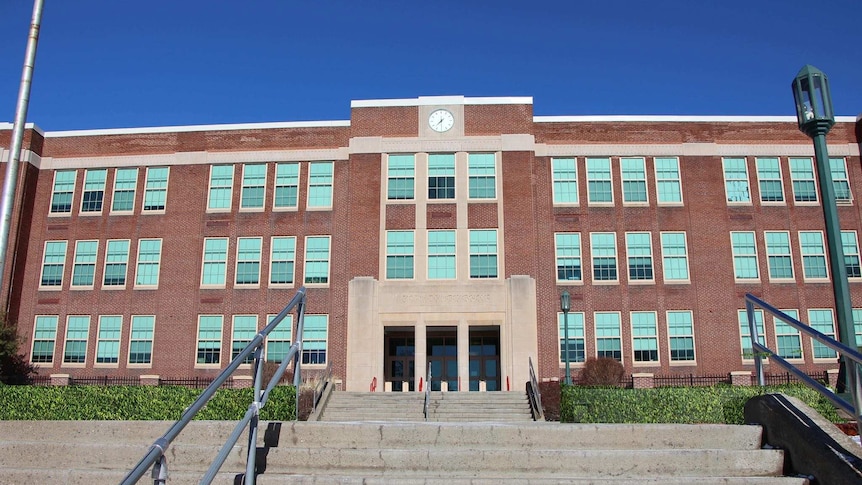 Image of the front of the East Middle School in Binghamton, New York. It is a big three storey red brick building with a clock.