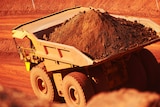 A BHP haulpak truck loaded with iron ore drives along a dirt mine road.