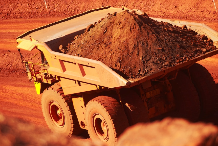 A BHP haulpak truck loaded with iron ore drives along a dirt mine road.