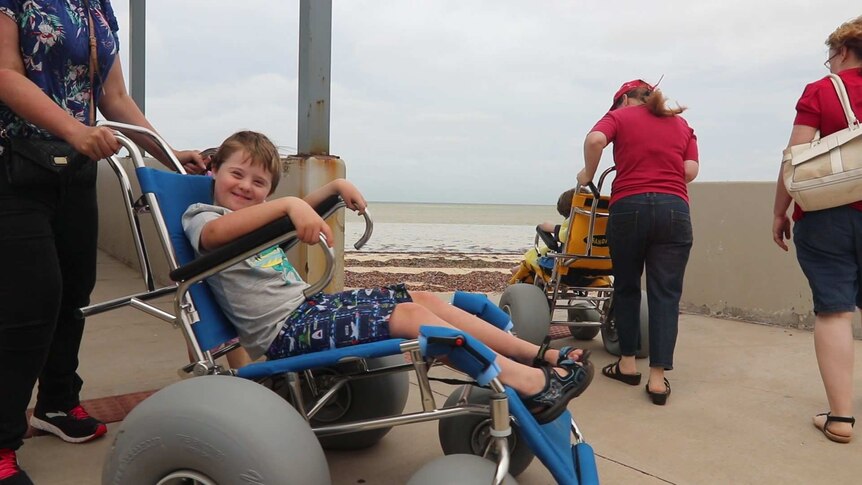 little boy smiling in wheelchair on left, wheelchair on the right