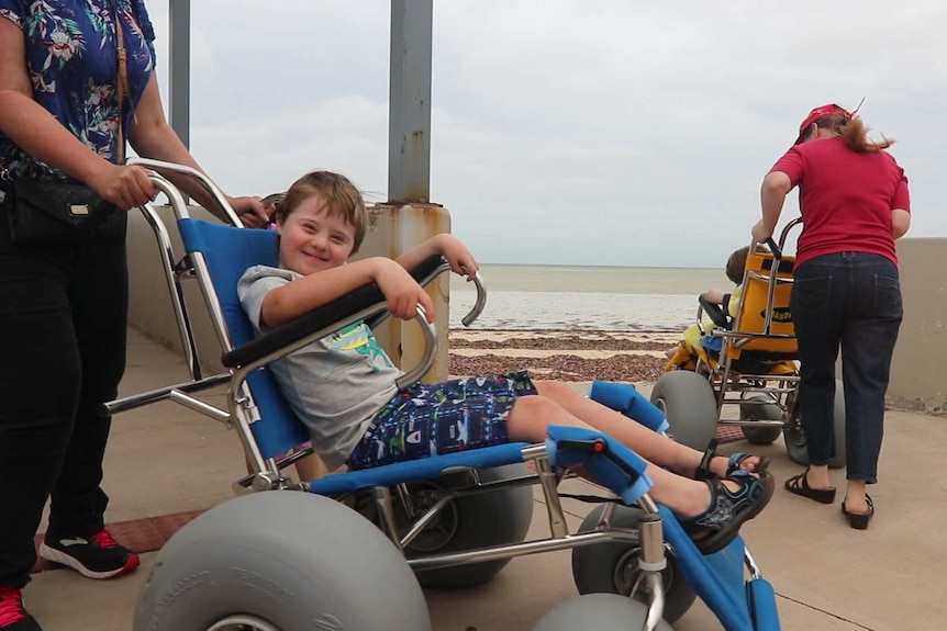 little boy smiling in wheelchair on left, wheelchair on the right