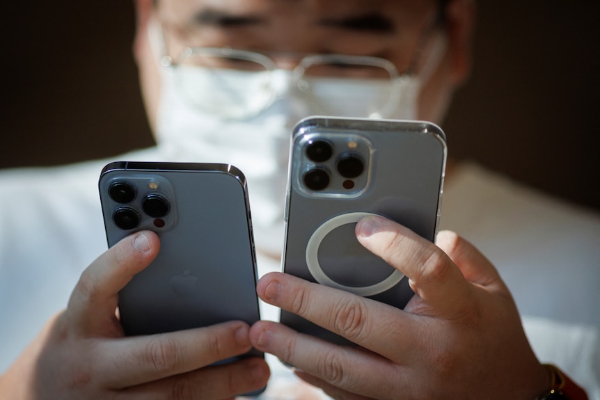 A man in a mask holding two iPhones. 