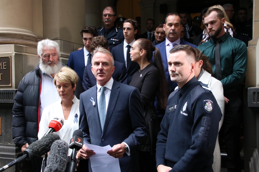 A group of people wearing suits stand outside court with solemn expressions on their faces.