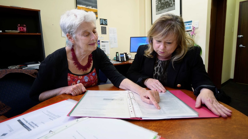 Two women sit at a table looking over documents.