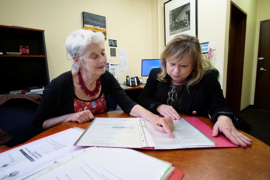 Two women sit at a table looking over documents.