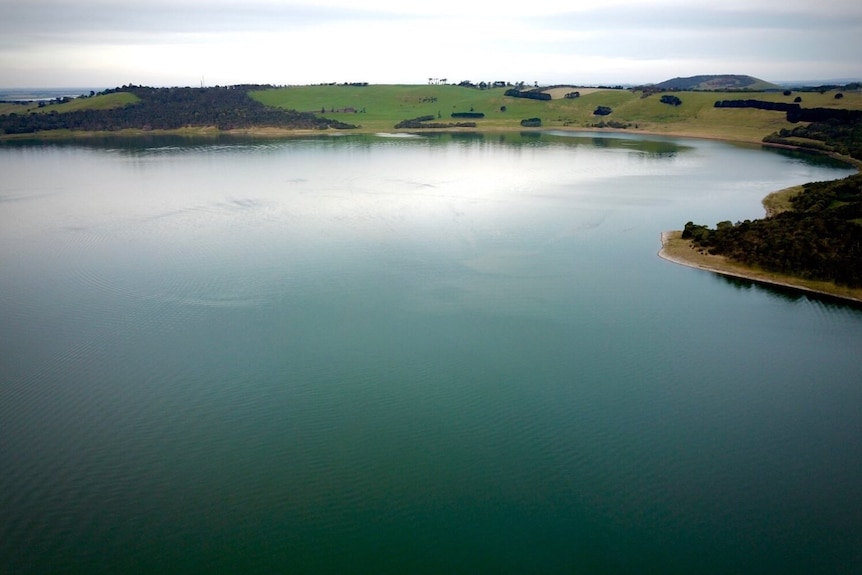 A beautiful teal coloured lake surrounded by grassy round hills spotted with a few trees