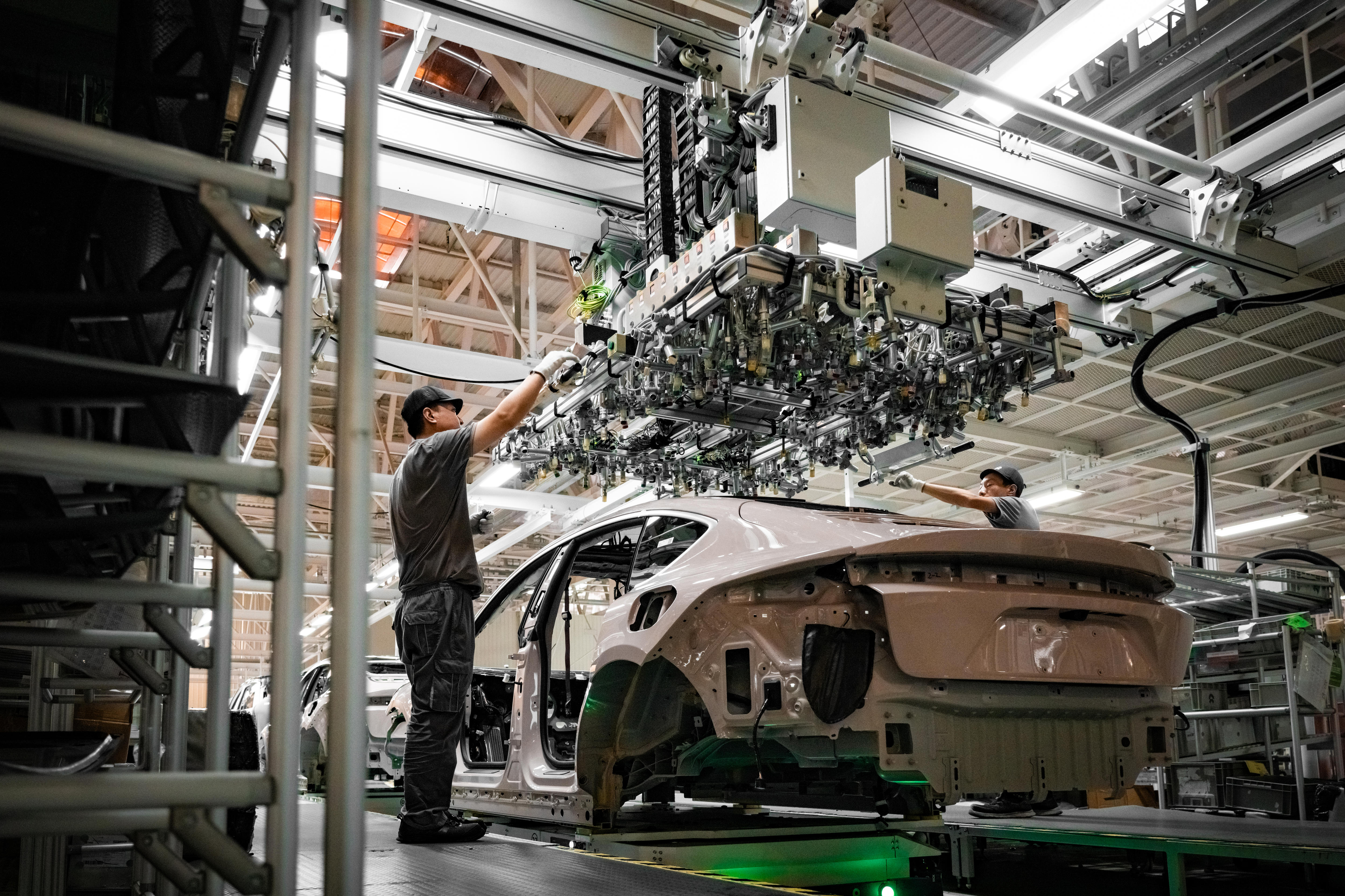 A man working on the manufacturing of a vehicle, with a large piece of machinery hovering over the vehicle.