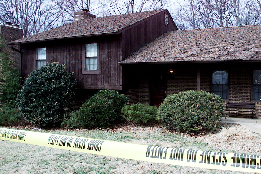 A dark wooden house is surrounded by police tape.