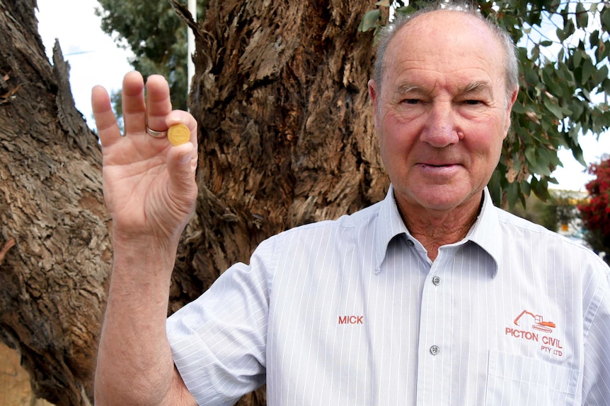 A man holding up a gold coin looking at the camera