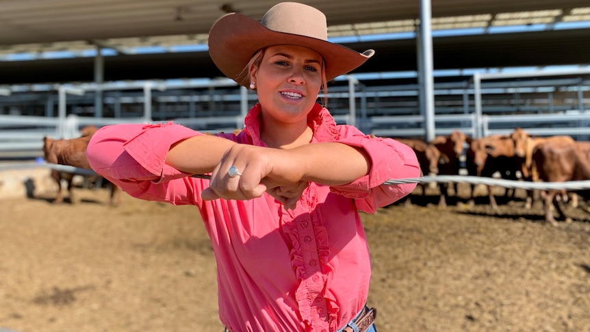 A girl stands in a hat and a pink shirt in front of some cattle