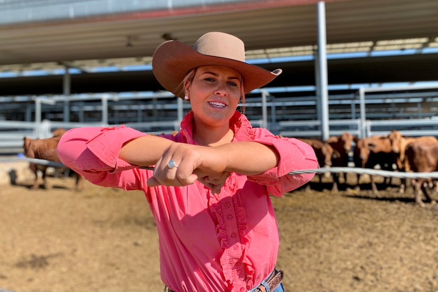A girl stands in a hat and a pink shirt in front of some cattle